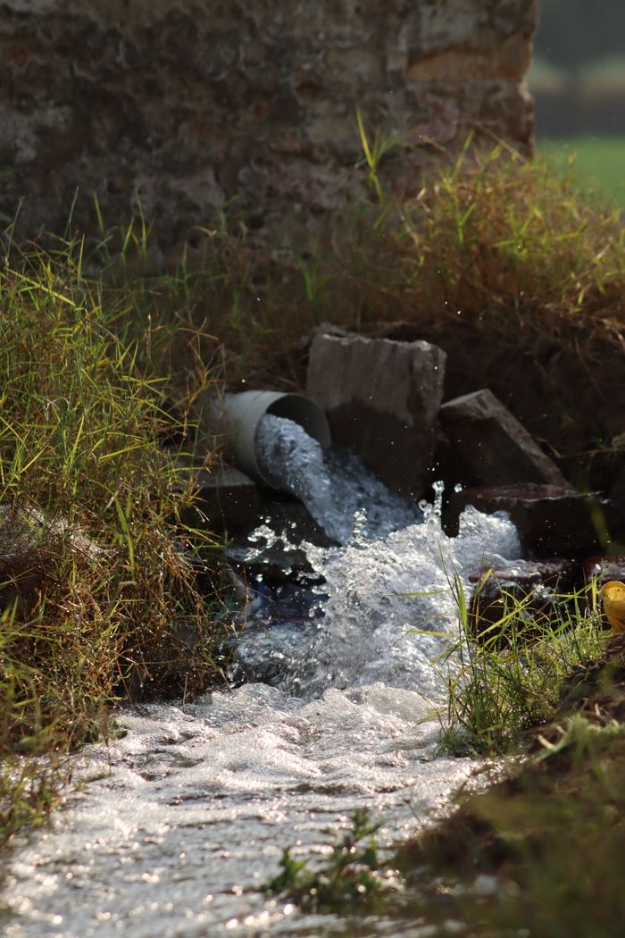 Vibrant water gushing from a rustic pipe into a grassy field, creating dynamic flow.