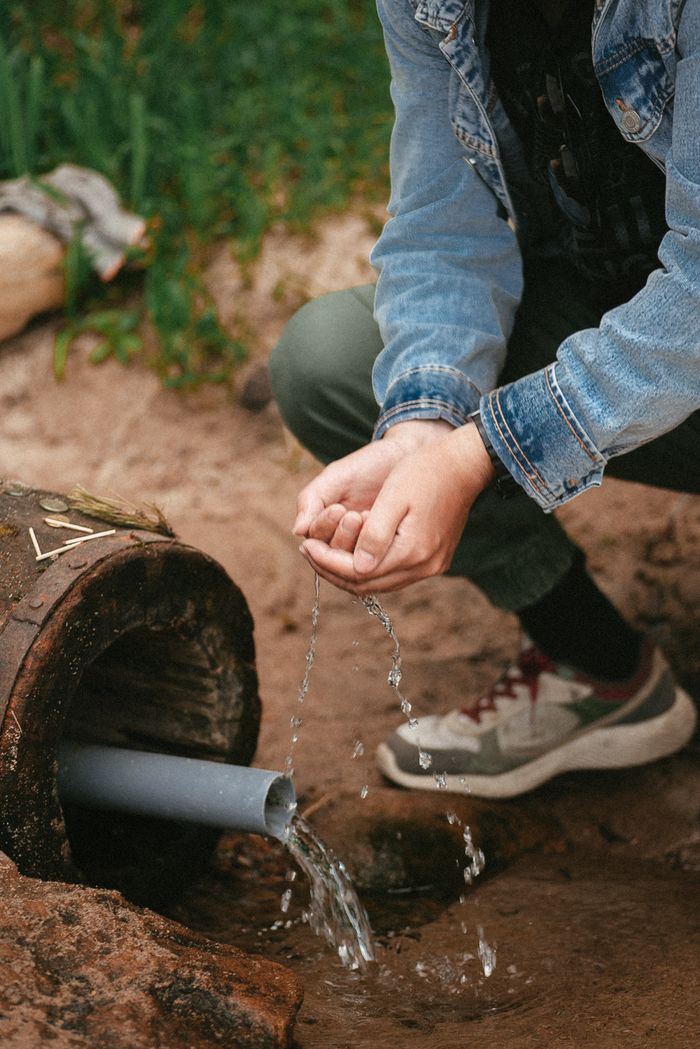 A person gathers fresh water from a natural source using bare hands outdoors.
